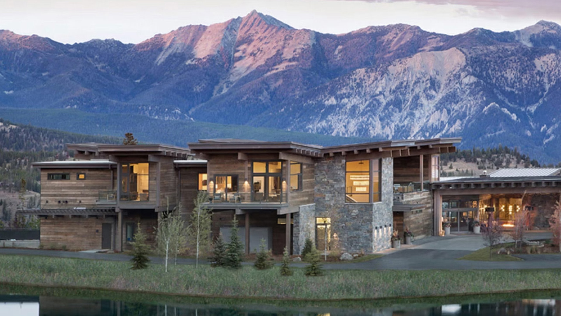 Modern mountain house with large windows and stone accents at dusk.