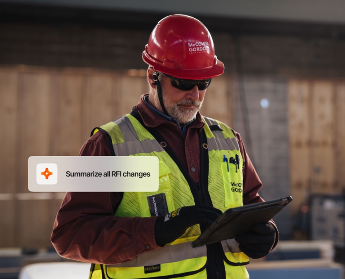 Construction worker in red hard hat and yellow safety vest holding tablet on job site