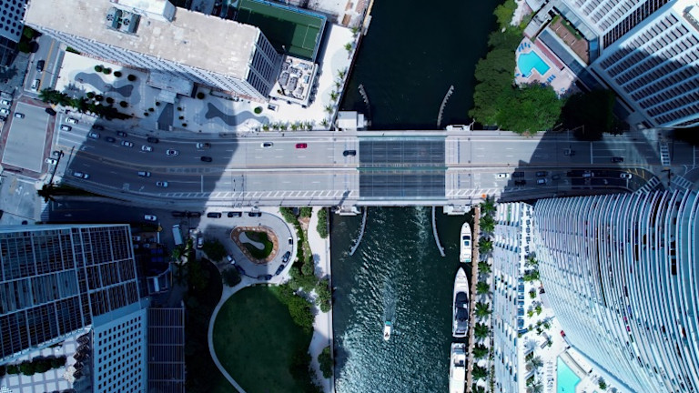 Aerial view of urban waterfront with bridge, buildings, and boats docked along water.