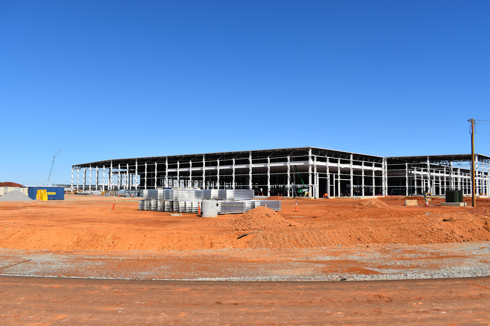 Industrial construction site with steel frame building under development on red dirt ground under clear blue sky