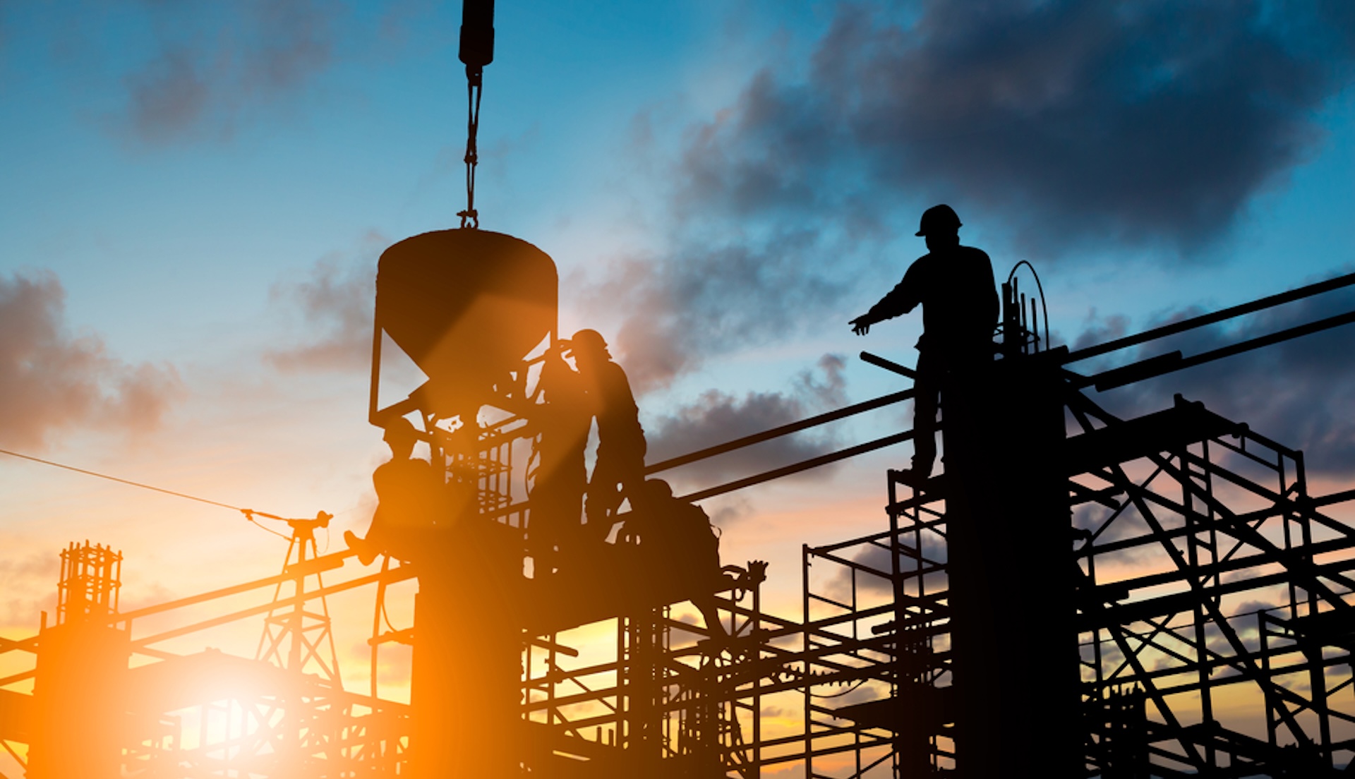Construction workers silhouetted on scaffolding.