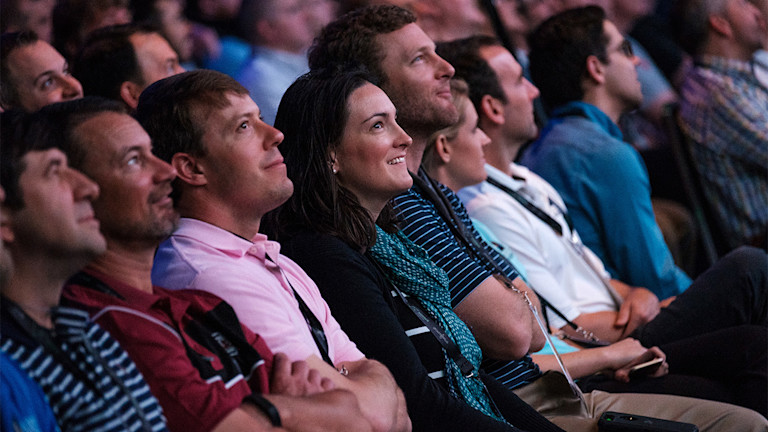 A group of people sitting in a row listening to a speaker