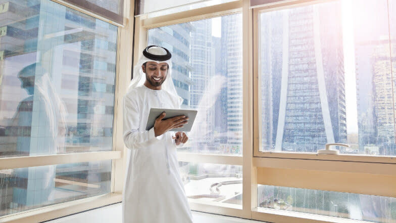 Men wearing a thobe standing inside of a glass building using a tablet