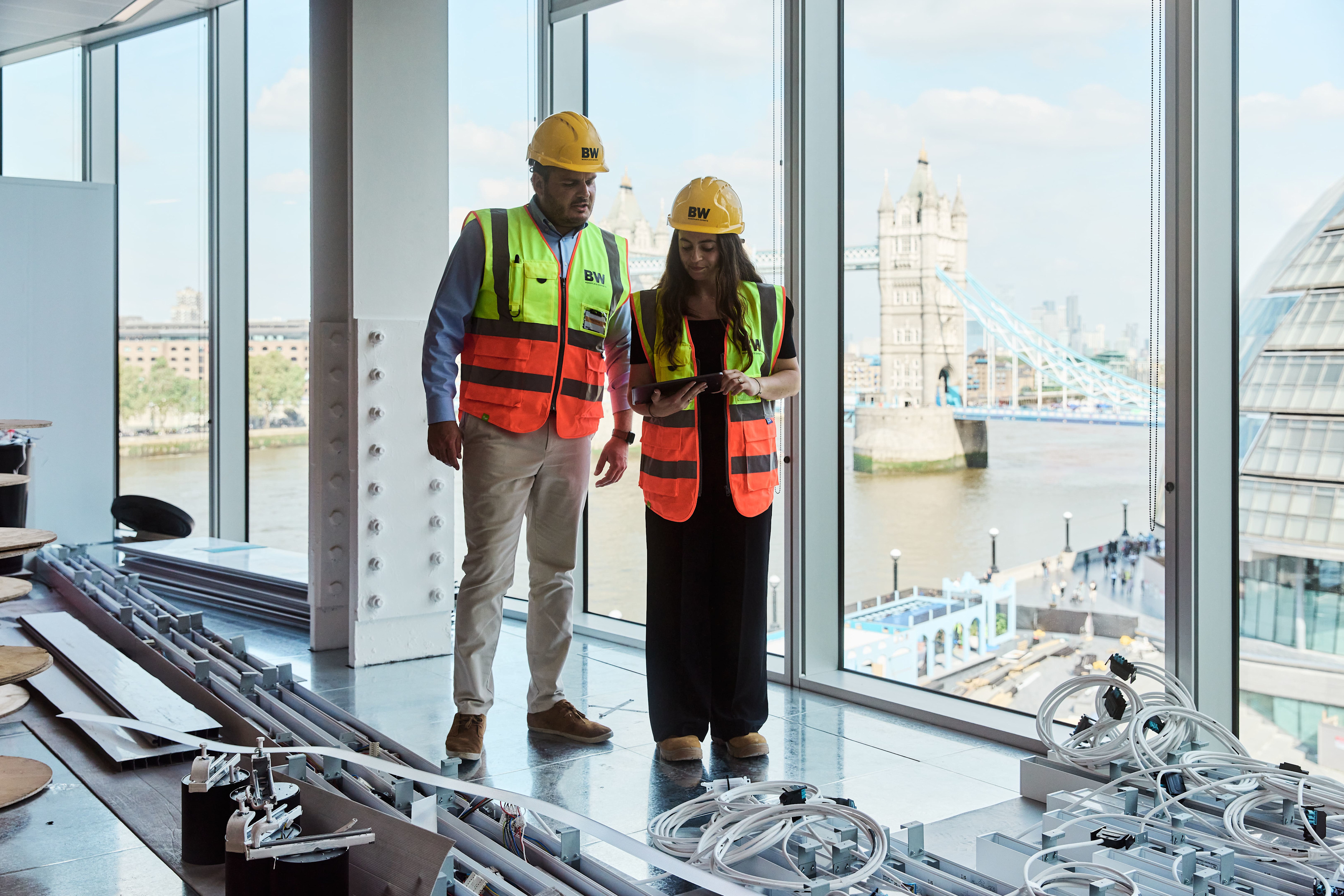 Two construction workers using a tablet while standing near a window of a building