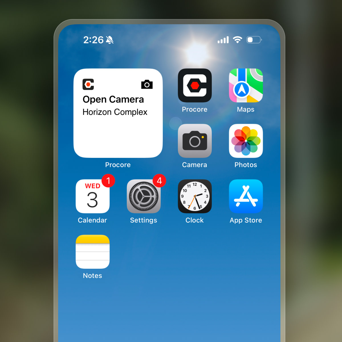 Smartphone home screen displaying various app icons including Procore, Camera, Maps, Photos, Calendar, Settings, Clock, App Store, and Notes.