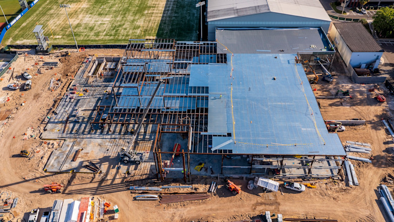 Aerial view of sports facility under construction with steel framing and blue roof covering.