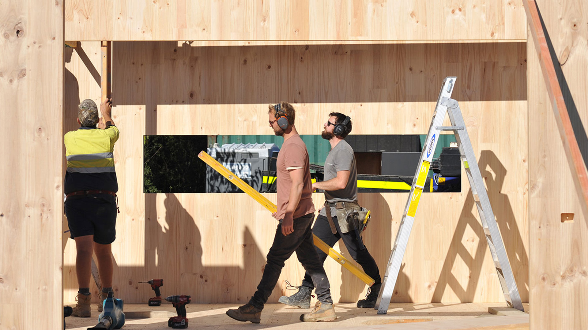 two men walking past a ladder and a wood wall