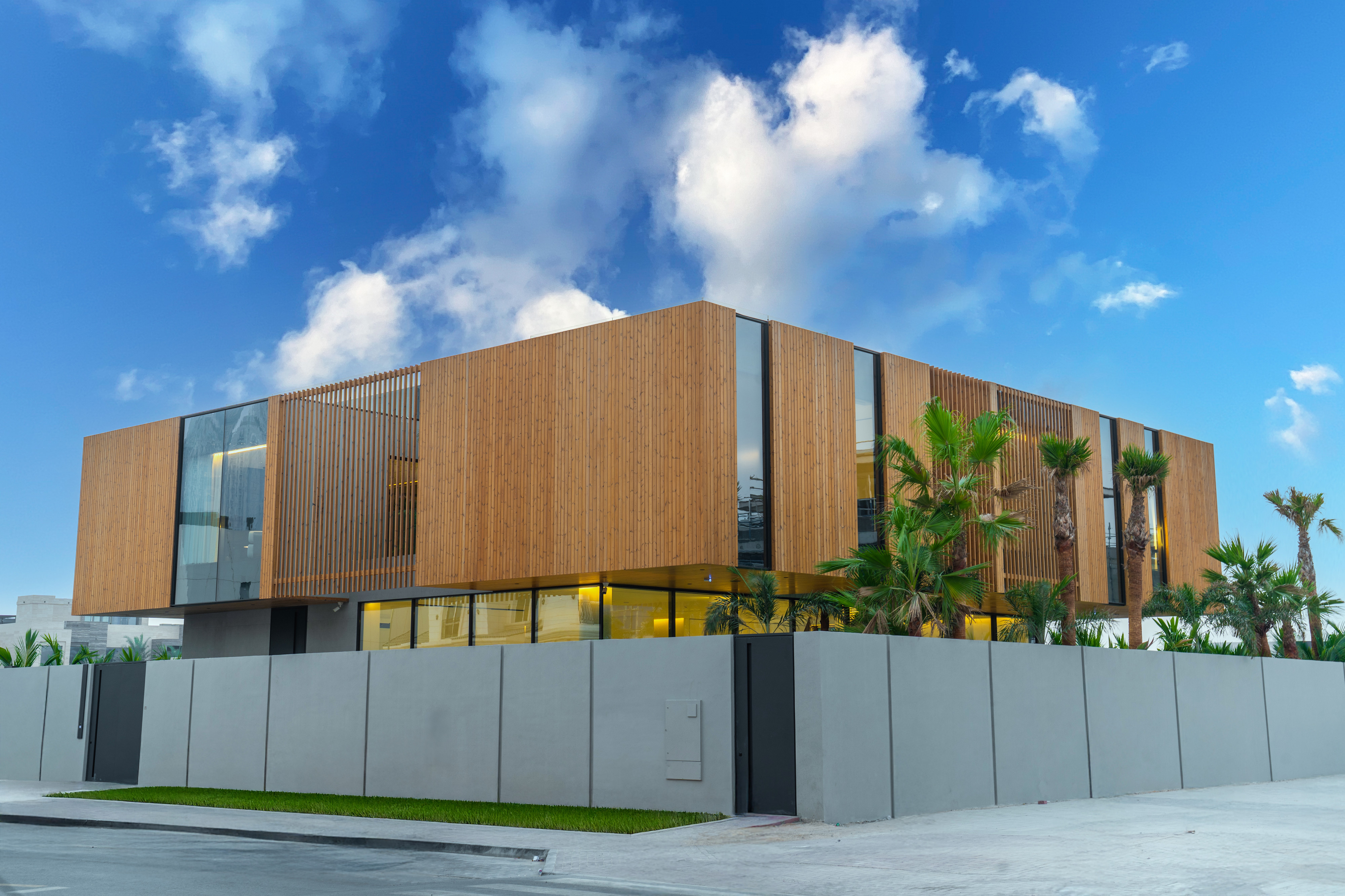 Modern two-story building with wooden panels, glass windows, and palm trees.