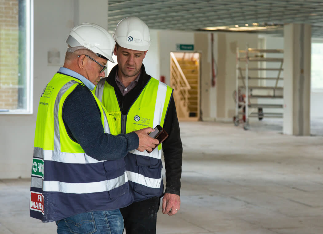 Construction worker colleagues looking at Procore software together on a device