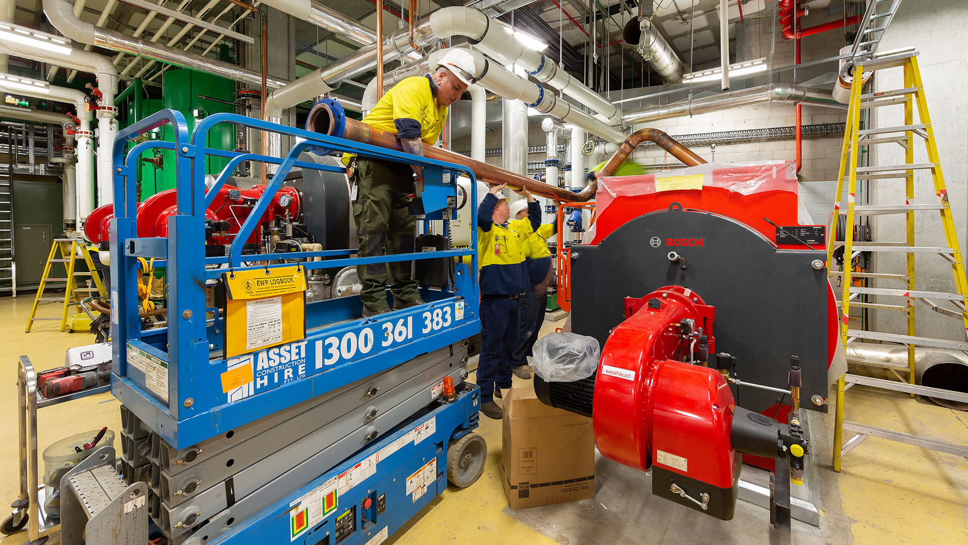 Two men moving a copper pipe next to a forklift.