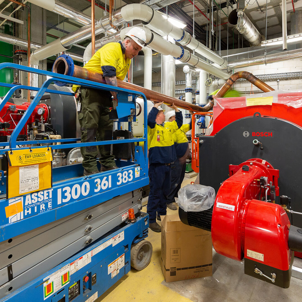 Two men moving a copper pipe next to a forklift.