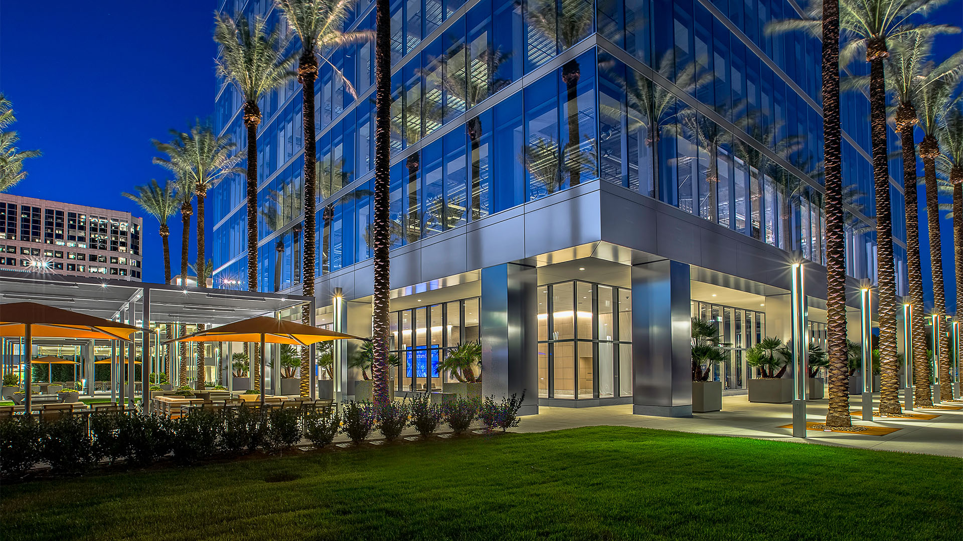 a glass building with palm trees and grass surrounding it