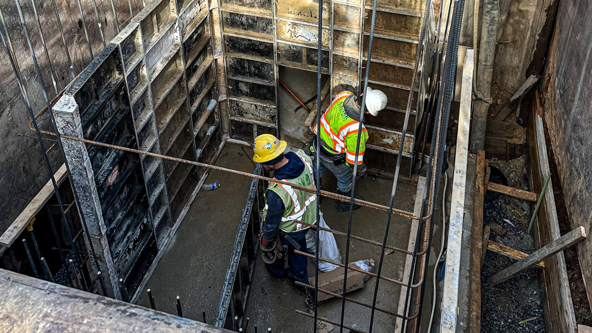 Two construction workers standing in a hole in a concrete area