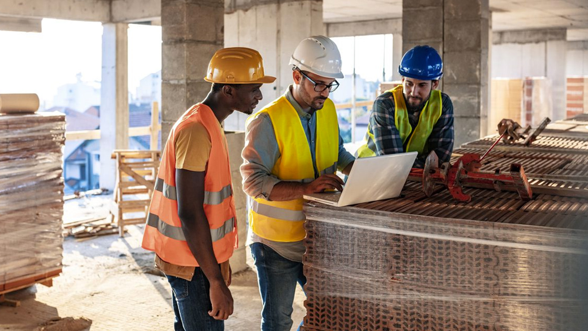 a group of men wearing hard hats and vests looking at a laptop