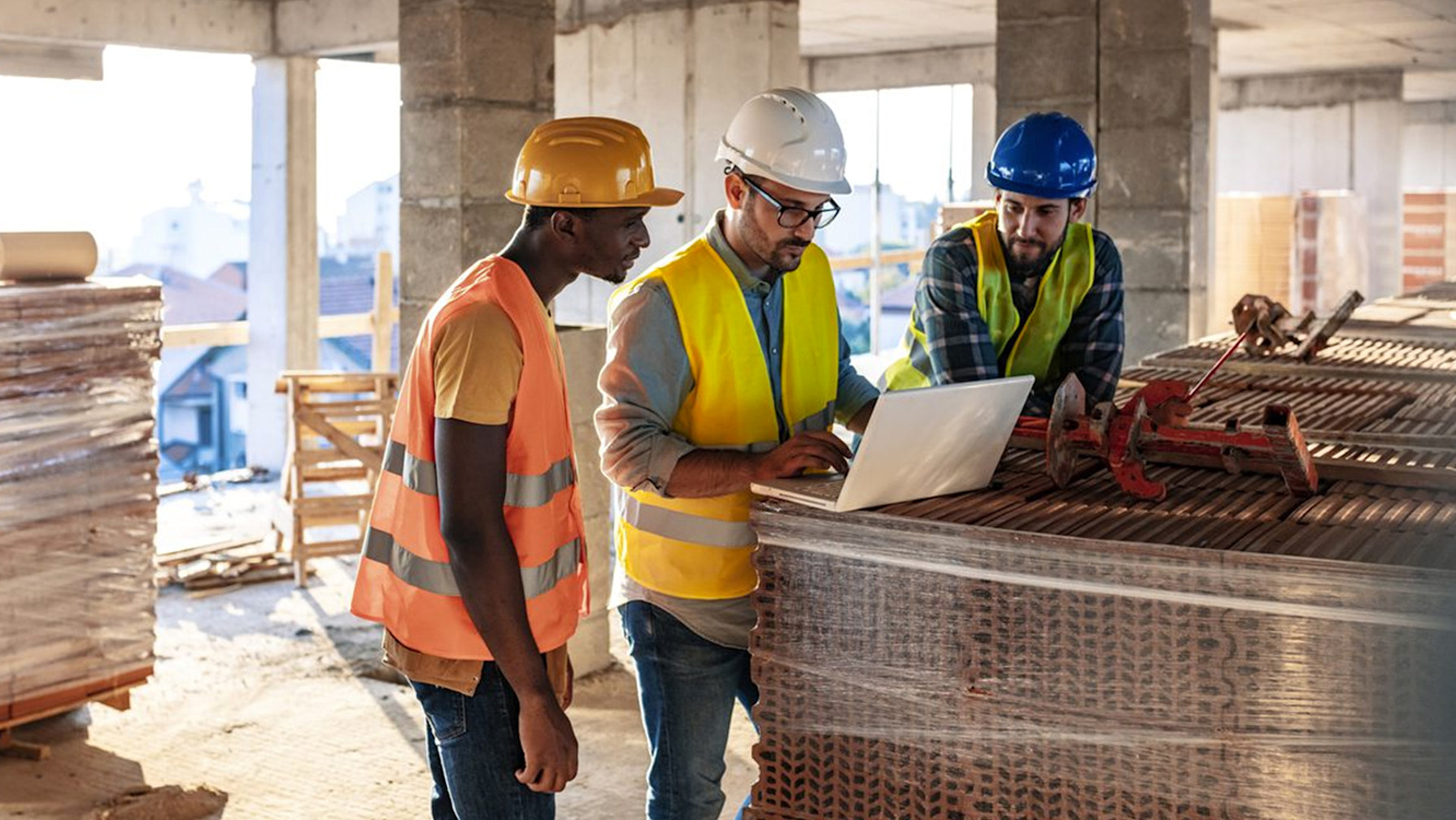 a group of men wearing hard hats and vests looking at a laptop