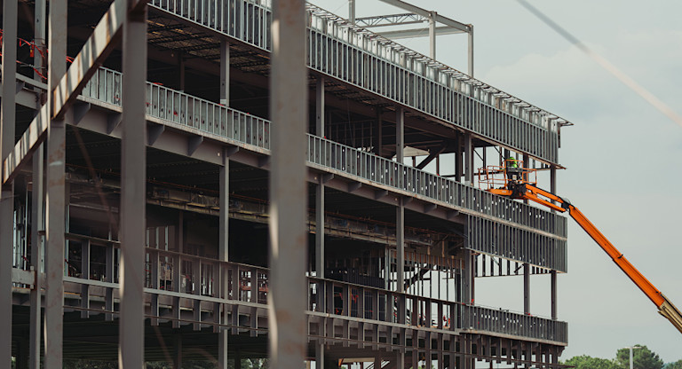 Construction worker on orange lift working on steel frame of building.