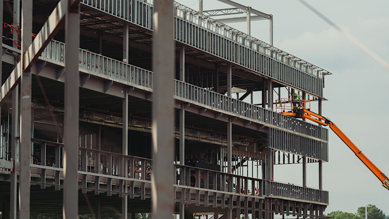 Construction worker on orange lift working on steel frame of building.
