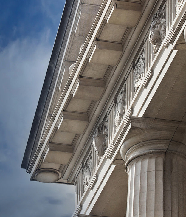 Ornate classical building facade with white columns and decorative stonework against blue sky.