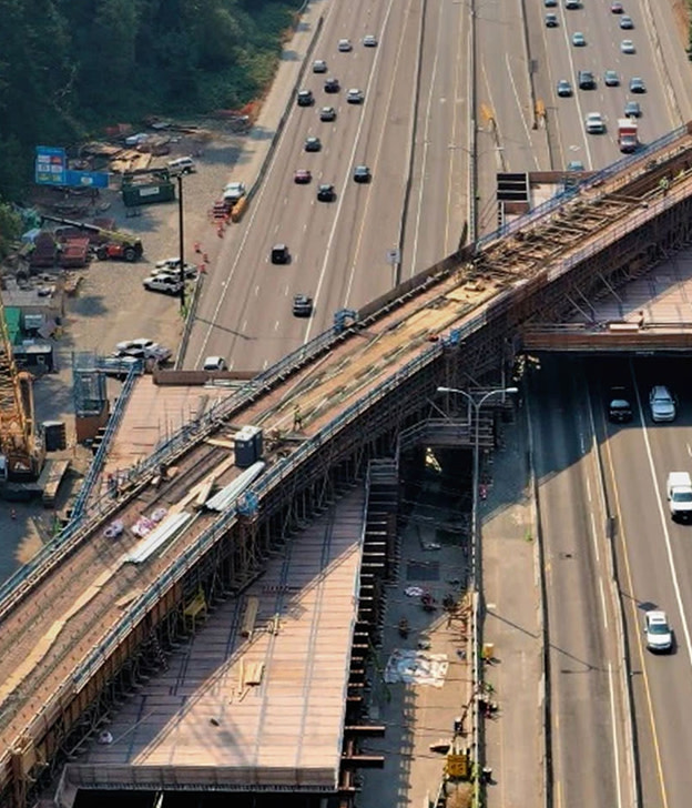 Aerial view of multi-lane highway with vehicles and elevated bridge structure under construction.