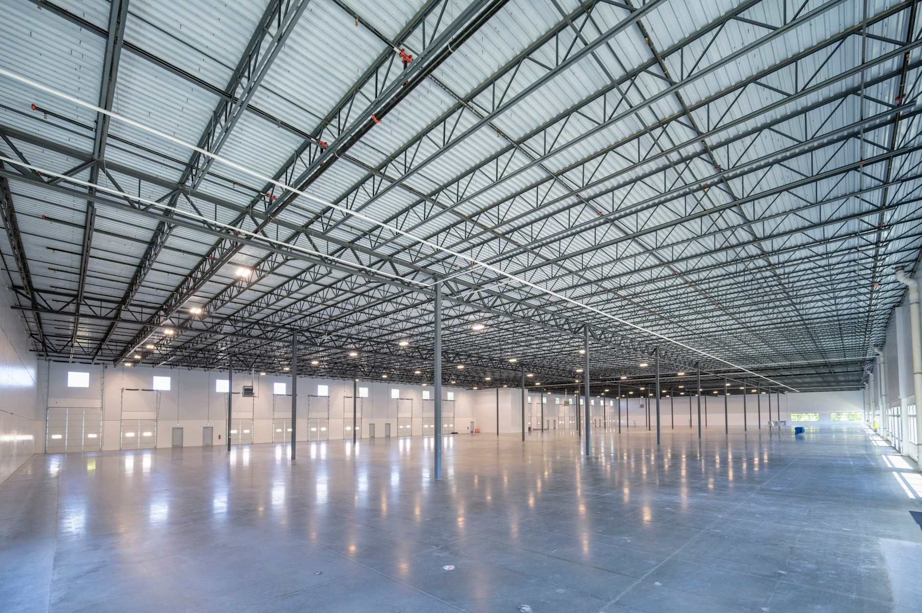 Empty industrial warehouse with polished concrete floor, steel beam structure, and metal roof panels with overhead lighting.