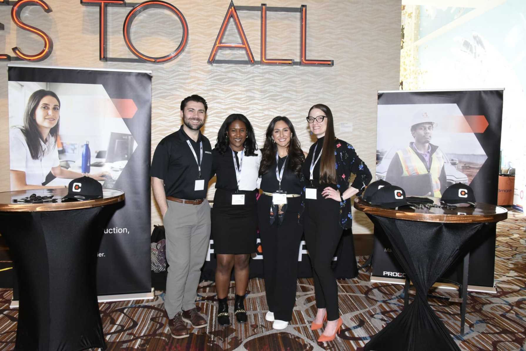 Four professionals smiling at a conference booth with promotional banners.