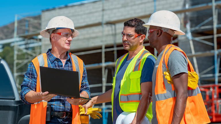 Contractors reviewing a project on a laptop while standing on site