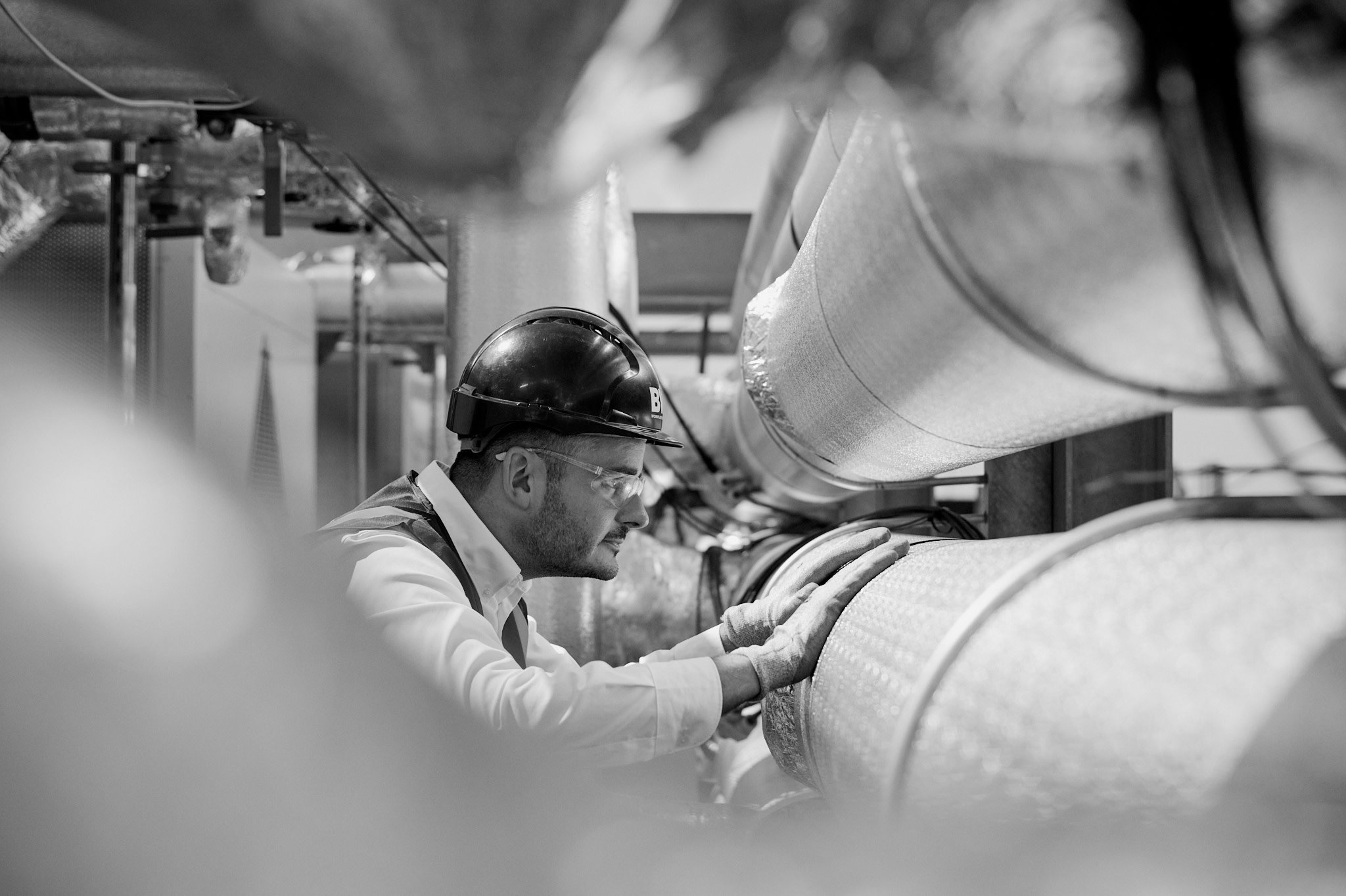 Man in hard hat inspecting large industrial pipes in a factory setting