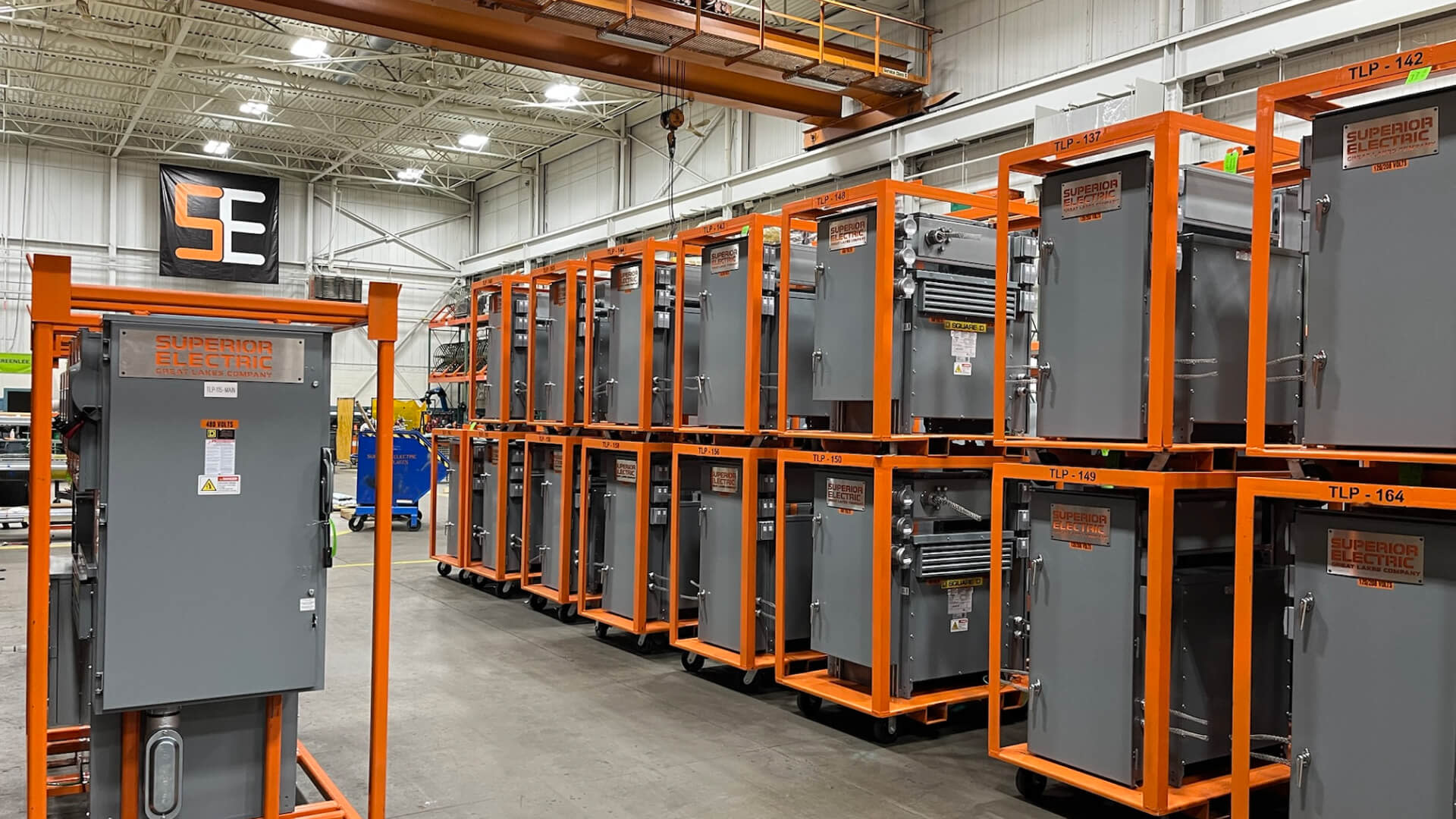 Electrical equipment organized on orange racks within a spacious warehouse setting