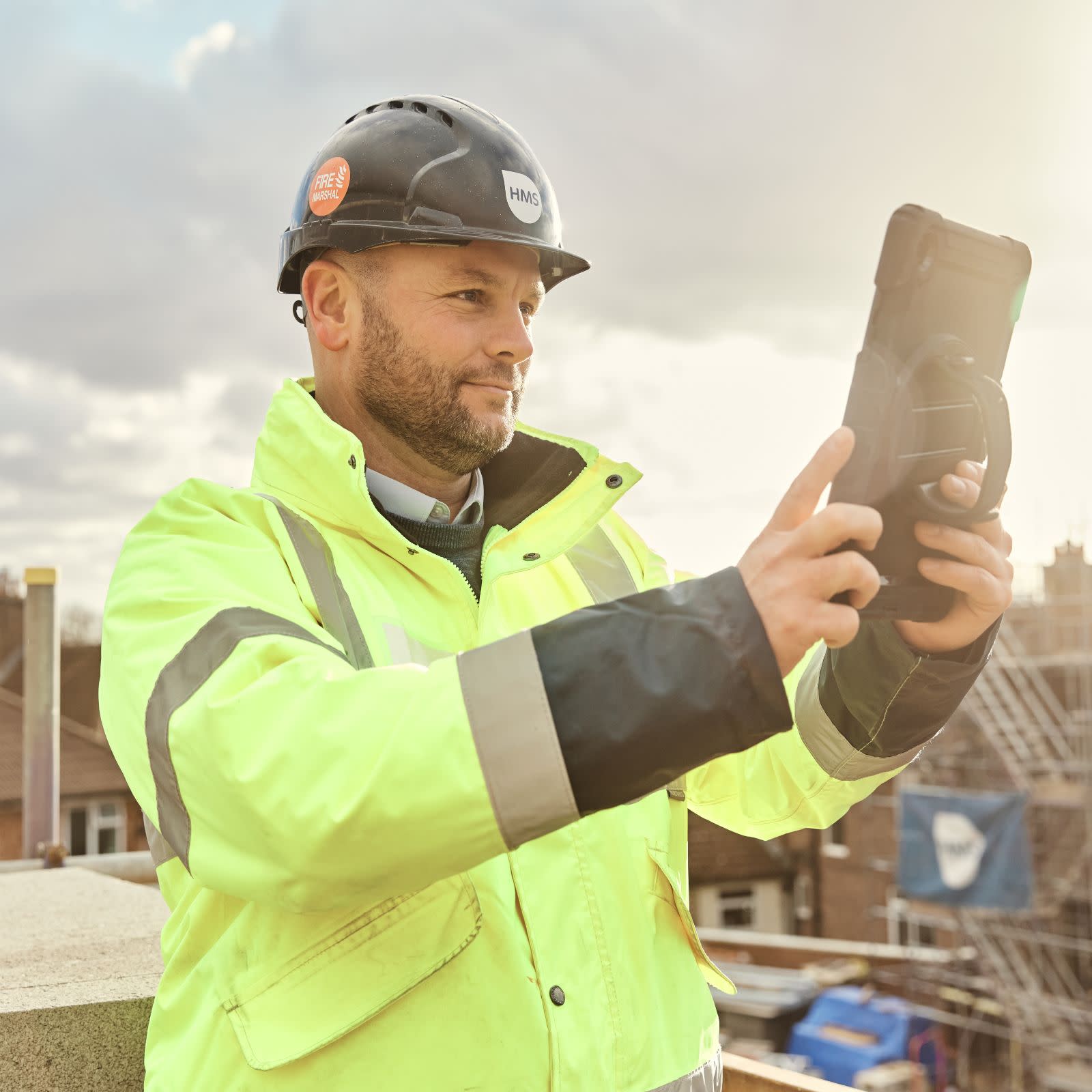 A man wearing safety gear holding a tablet on a jobsite