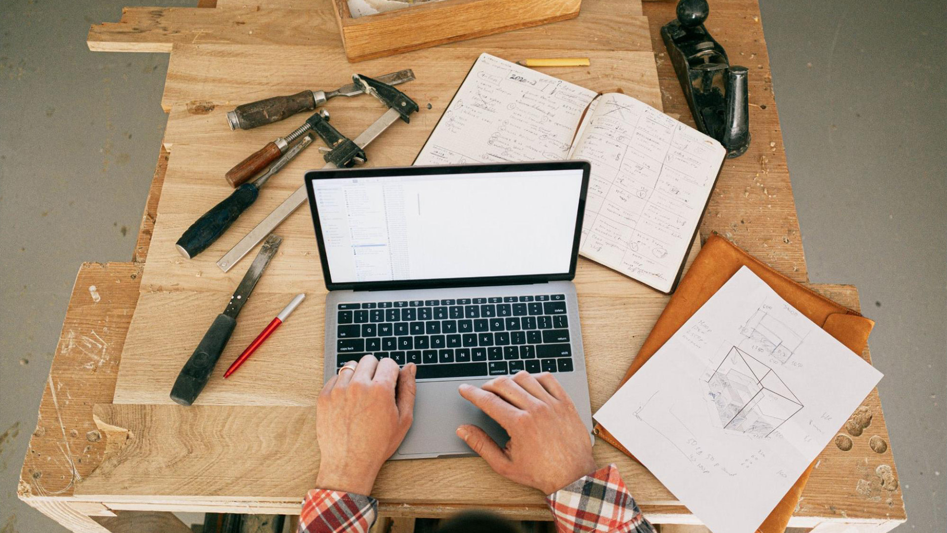 A table with notebooks and tools and a person using a laptop
