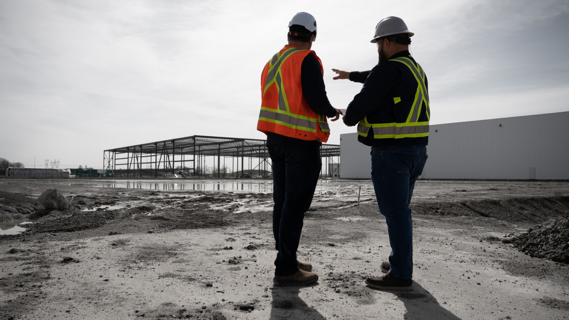 Two men standing on a construction site, pointing to the construction