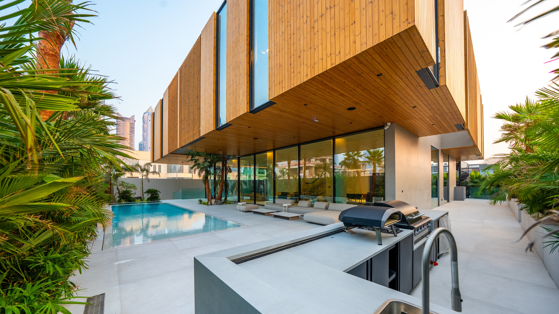 Modern house with wooden facade, outdoor pool, lounge chairs, and grill area.