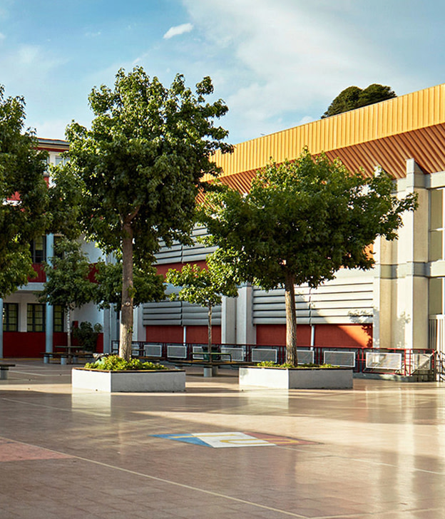 Modern courtyard with trees, industrial building with yellow metal roof and red accents under blue sky