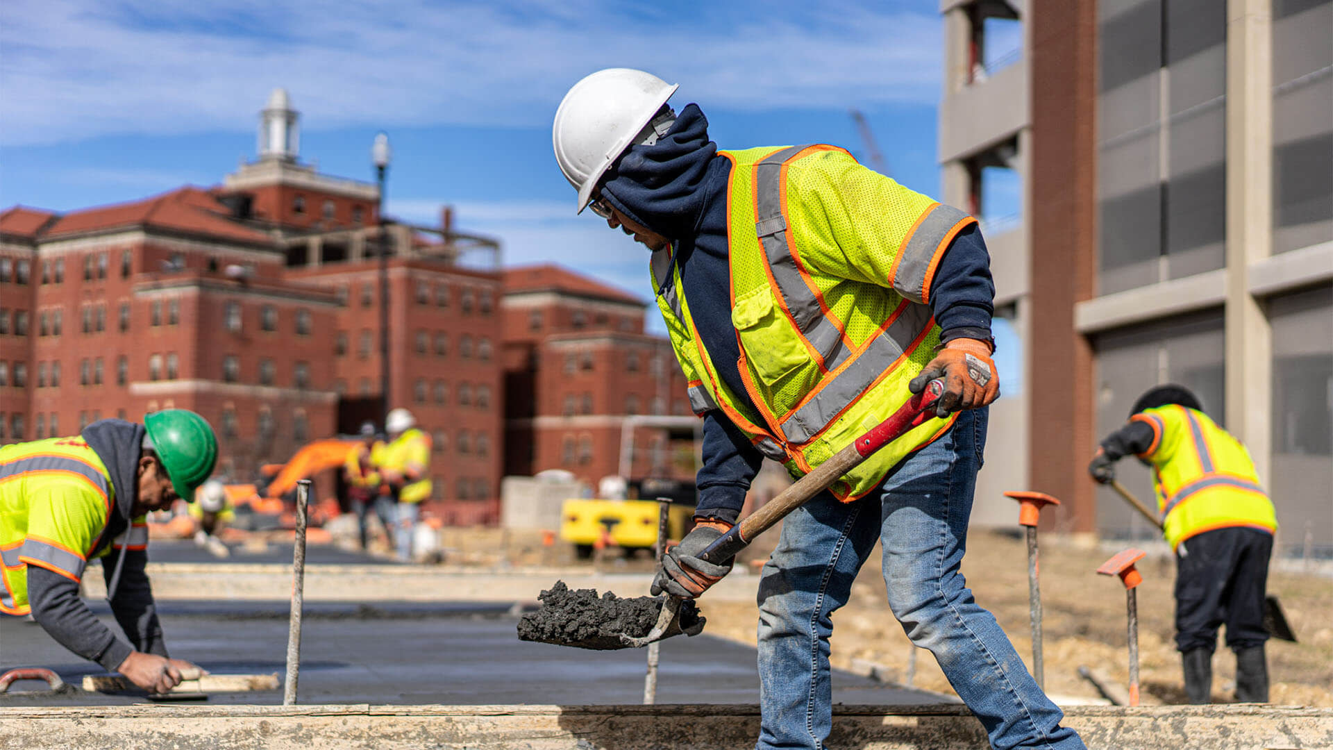 A man in a safety vest and helmet using a shovel to flatten cement