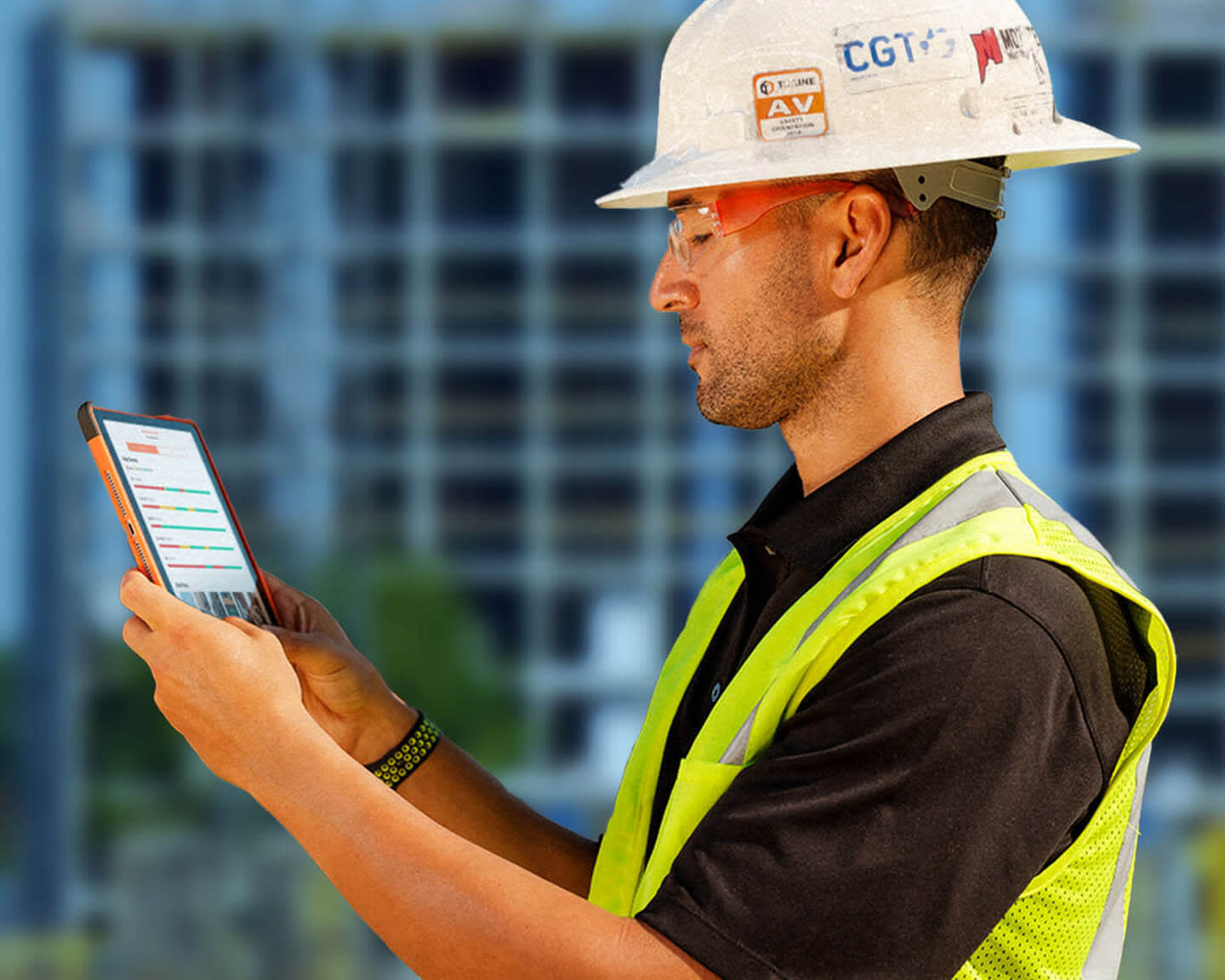 A man wearing safety gear holding a tablet on a construction site