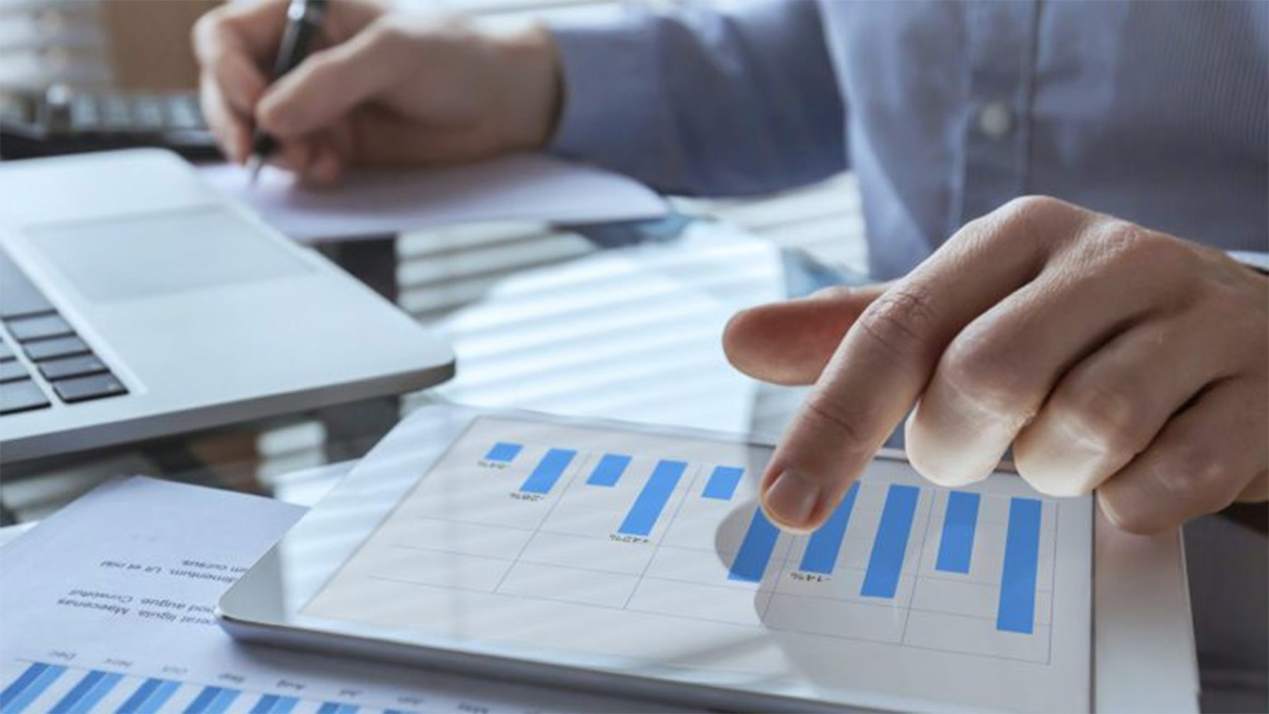 A person writing in a piece of paper and looking at graphs in a tablet