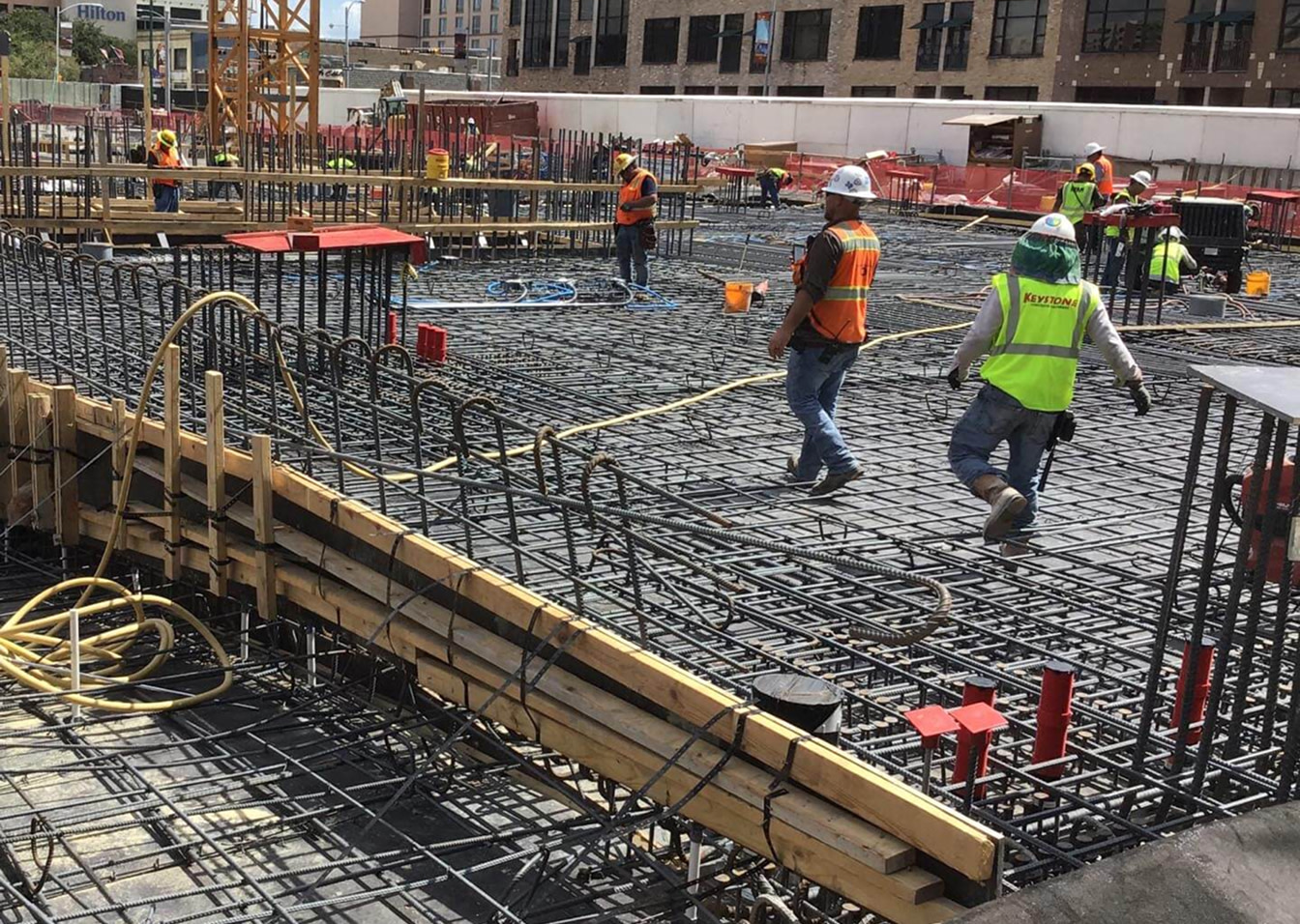 Construction workers in safety gear walking on steel rebar grid at site.