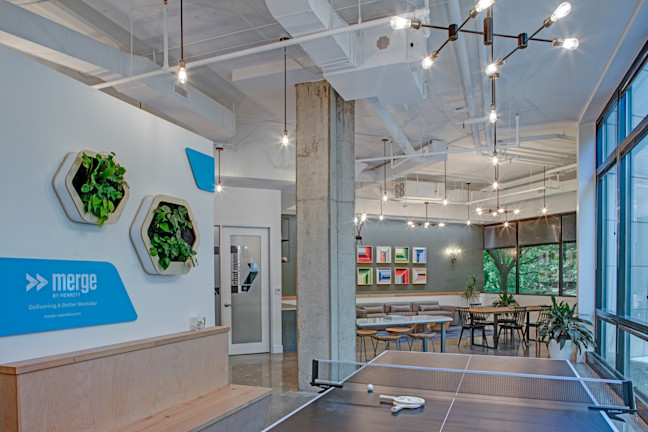 Modern office lobby with Merge branding, hanging plants, ping pong table, and lounge area with colorful shelving.