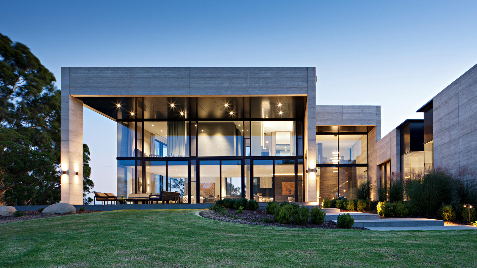 Front view of a mostly glass house with mini patch of lawn at the front.