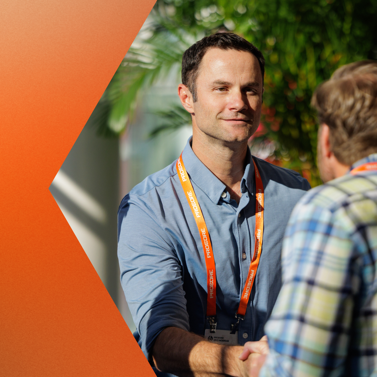 Man in blue shirt wearing orange lanyard badge shaking hands outdoors