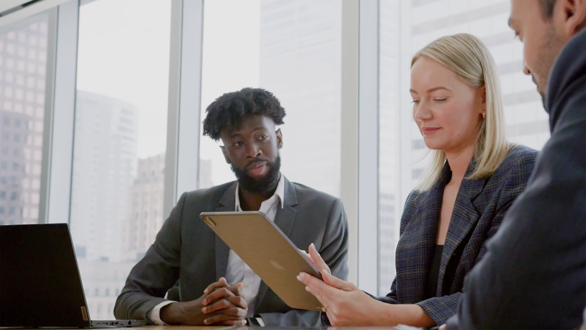 Business professionals reviewing documents in modern office with city skyline view through windows.