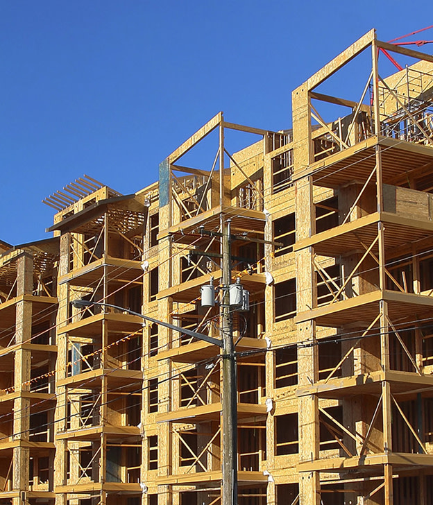 Multi-story wooden building frame under construction against clear blue sky