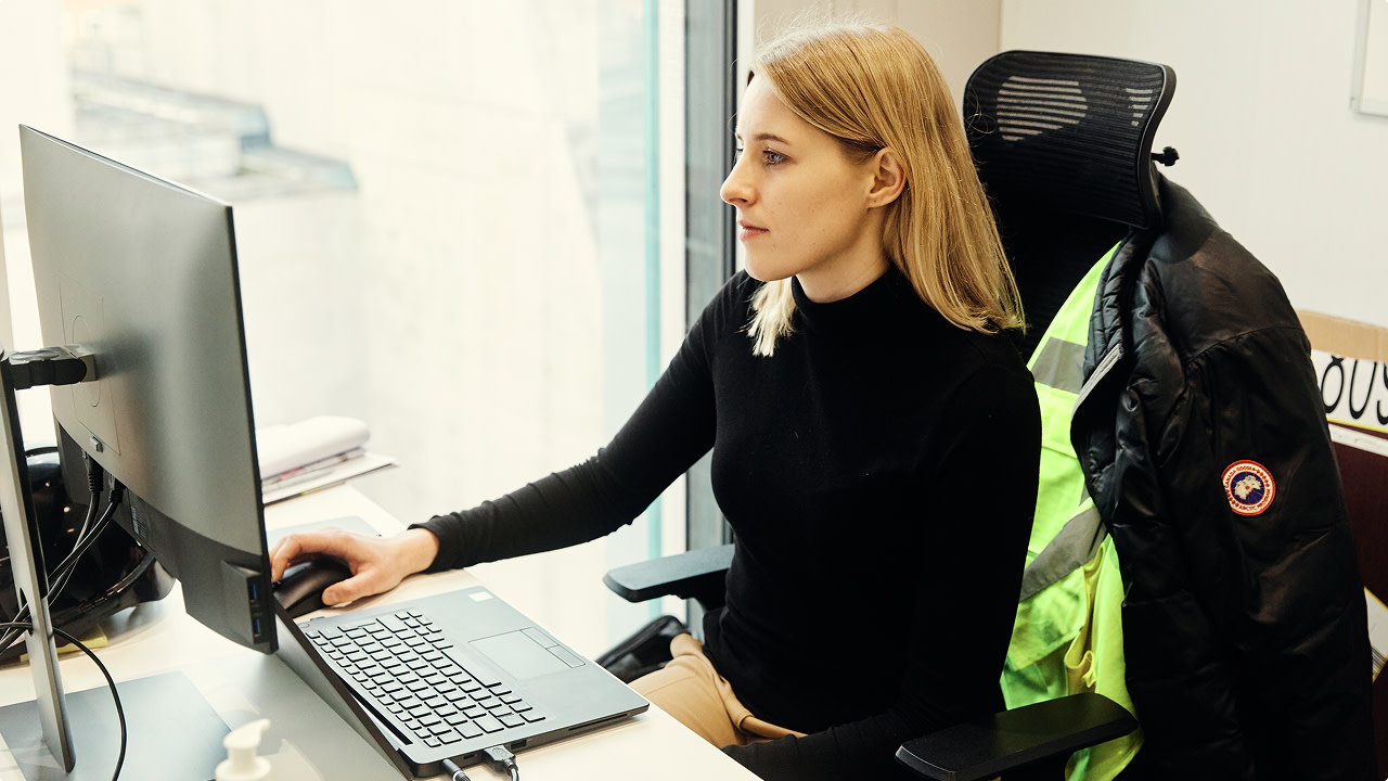 Woman in black sweater working on a computer at a desk by a window.