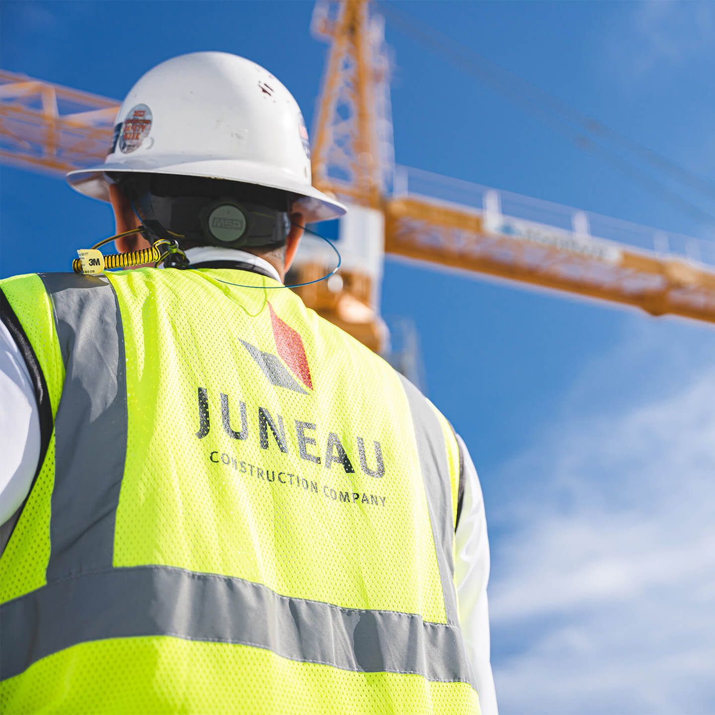 A Juneau contractor wearing a safety vest and a hard hat looking at a crane