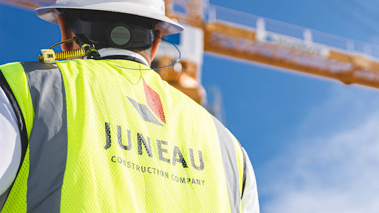 A Juneau contractor wearing a safety vest and a hard hat looking at a crane