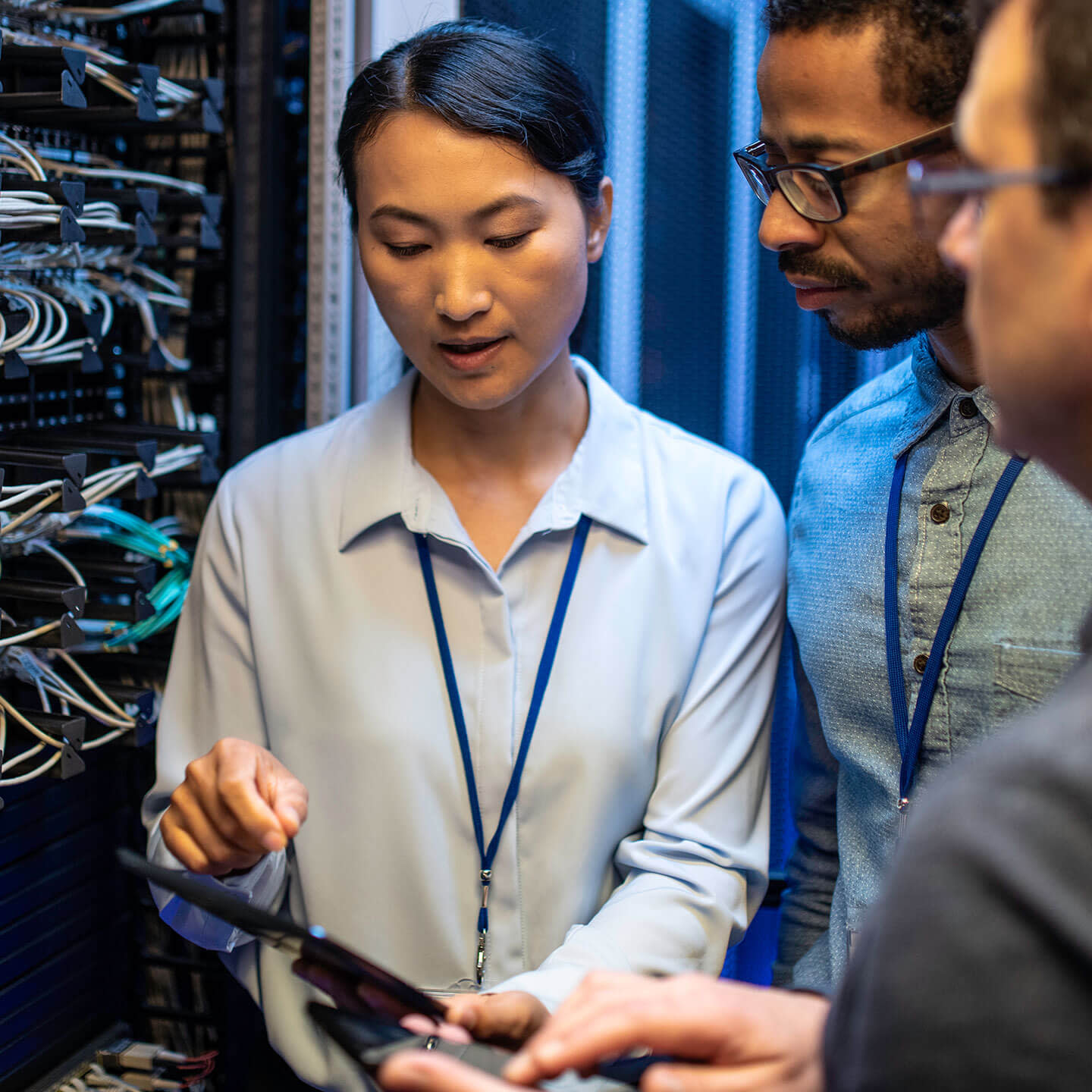 three people standing in front of server racking, reviewing information on a tablet