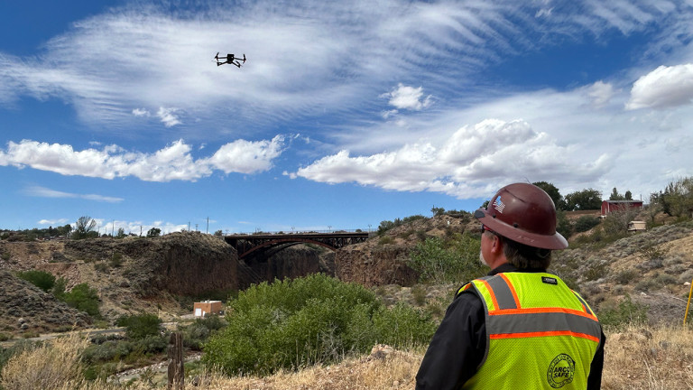 A construction worker looking at a drone flying over a hill