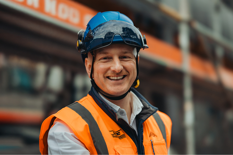 Smiling construction worker wearing blue helmet and orange safety vest.