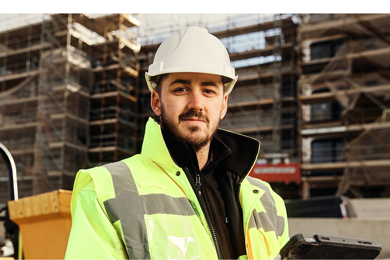 Construction worker in a white helmet and yellow jacket at site.