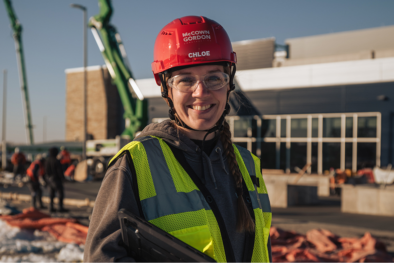 Smiling construction worker wearing red helmet and yellow vest outdoors.